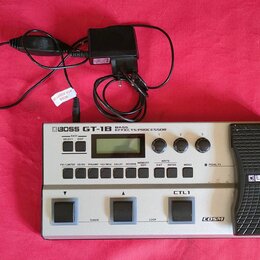 Stříbrný basový efektový procesor s černým pedálem, na kterém je nápis BOSS GT-1B BASS EFFECTS PROCESSOR. Na přístroji jsou vidět ovládací knoflíky,…