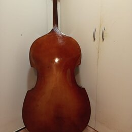 Fotografie zachycuje zadní stranu smyčcového nástroje, pravděpodobně violoncella, v hnědém lakovaném provedení. Nástroj je vyroben ze dřeva a vykazuj…