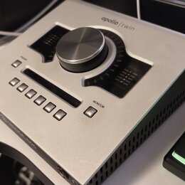 Stříbrný audio rozhraní s velkým centrálním ovládacím knoflíkem. Na horní straně je nápis apollo | twin a v dolní části logotyp UNIVERSAL AUDIO. Zaří…