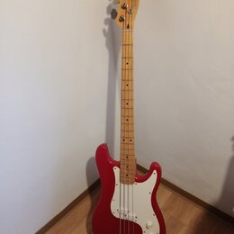 Červená elektrická basová kytara s bílým pickguardem a hřednou z jasného dřeva. Na hlavě je nápis "Fender Jazz Bass". Nástroj vykazuje běžné známky p…