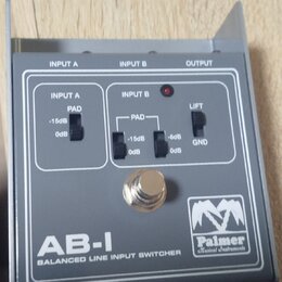 Šedý kovový přístroj s nápisem AB-I BALANCED LINE INPUT SWITCHER a logem Palmer Musical Instruments. Na horní straně jsou označení INPUT A, INPUT B a…