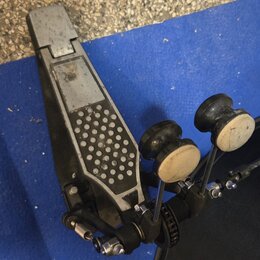 Fotografie zachicuje černý pedál bicího bubnu s šedým, texturovaným stupněm. Na mechanismu nejsou viditelné žádné značky ani nápisy. Povrch stupně vy…