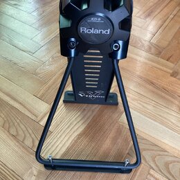 Černý elektronický basový pad na kovovém stojanu. Na přední straně je bílý nápis Roland a nad ním štítek s textem KD-8 KICK TRIGGER PAD. V dolní část…