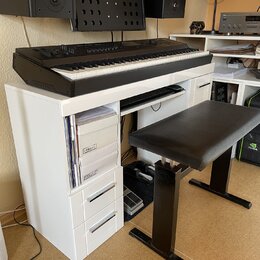 Černý digitální klavír umístěný na bílém stole s přihrádkami. Na levé straně klavíru je nápis MONTREUX. K sestavě patří černá polstrovaná piano stoli…