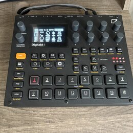 Černý digitální sampler Digitakt II s displejem a ovládacími prvky. Na přední straně je nápis Digitakt II a řada tlačítek, otočných knoflíků a vstupn…