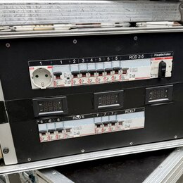 Černý rozvodový panel v hliníkovém flightcasu. Panel obsahuje elektrické zásuvky, jističe a tři digitální voltmetry s červeným displejem. Jsou zde ná…