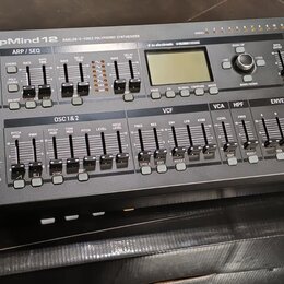 Černý polyfonní syntetizátor s nápisem DeepMind 12 ANALOG 12-VOICE POLYPHONIC SYNTHESIZER. Na předním panelu jsou vidět knofíky, tlačítka a displej s…