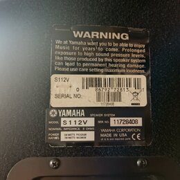Detailní záběr na zadní stranu černého reproduktoru s dvěma nálepkami. Horní nálepka obsahuje varovný text „WARNING“ a označení „S112V“, čárcový kód…