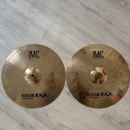 Dvě mosazné činely typu hi-hat položené vedle sebe na světlé podlaze. Oba mají identické nápisy: v horní části „IMC 13" BRILLIANT HI-HAT“ a v dolní č…
