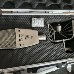 V otevřeném hliníkovém kufru s černou pěnovou výplní je umístěn stříbrný mikrofon a kovový shock mount. Na těle mikrofonu je vidět logo SE a označení…