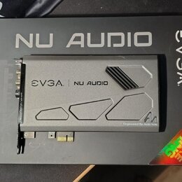 Šedá zvuková karta s kovovým krytem, položená na černém kartónovém obalu. Na krytu i na obalu je uveden nápis EVGA NU AUDIO a v pravém dolním rohu kr…