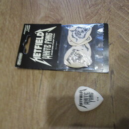Sada kytarových trzelíků v originálním balení a jeden samostatný trzelík. Na černém obalu je bílý nápis METALLICA WHITE FANG CUSTOM FLIGHT PICK. Samo…