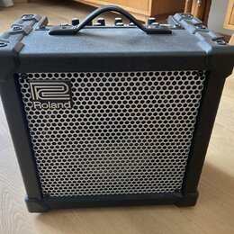Černý kombo zesilovač s kovovou mřížkou reproduktoru. Na přední straně je umístěno logo a nápis Roland. Horní strana obsahuje ovládací prvky a přenos…