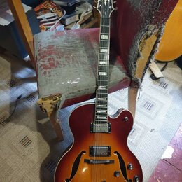 Polodublová elektrická kytara s červeně-žlutým sunburst povrchem a f-otvory. Na hlavě je bílý nápis „Kay Raven“. Kytara má dva snímače, tři ovládací…