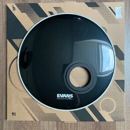 Černý bubenový kožen s bílým okrajem, umístěný na kartonovém podkladu. V dolní části je bílý nápis EVANS a pod ním menší text BRANDED HEADS. Povrch j…