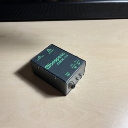 Černý kovový efekt pedál s nápisy v zelené barvě. Na horní straně je logo a název Bespeco a model DBX-10. Na boku jsou viditelné popisky vstupů a výs…