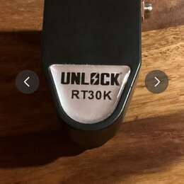 Černý kytarový pedál s kovovým štiťkem. Na přední straně je stříbrný štítek s nápisem UNLOCK RT30K. Povrch je matně černý, v horní části je vidět kno…