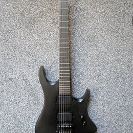 Černá elektrická kytara s matným povrchem a ostře hranatým tvarem těla. Nástroj má dva humbuckery, jeden ovládací knoflík hlasitosti a hmatník bez vi…