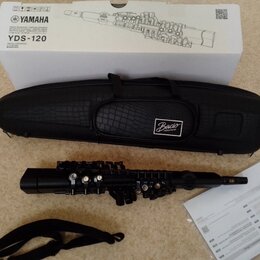 Na fotografii je digitální saxofon černé barvy, černý obal s texturou kůže a bílý kartonový box. Na krabici je nápis YAMAHA a model YDS-120. Na obalu…