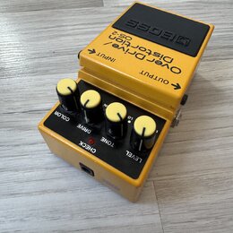 Žlutý kytarový efekt s černým horním panelem, na kterém je nápis BOSS. Na těle jsou texty OverDrive/ Distortion OS-2 a označení vstupů INPUT a OUTPUT…