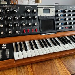 Synthesizér s klaviatura v dřevěném šasi. Na horním ovládacím panelu jsou nápisy LFO, MODULATION BUSSES, OSCILLATORS, MIXER, FILTERS, ENVELOPES a OUT…
