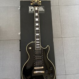 Černá elektrická kytara s bílým lemováním, položená na černém kufru s nápisem PAUL REED SMITH GUITARS. Na hlavě kytary je zlaté logo s nápisem Paul R…