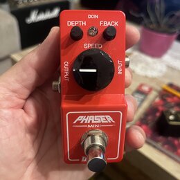 Červený kytarový efekt pedál s nápisem PHASER MINI. Na horní straně jsou dva malé černé otočné oválky s popisky DEPTH a F.BACK, velký černý ovládací…