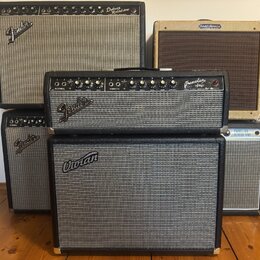Fotografie zobrazuje čtyři kytarové komba. V horní části jsou dva zesilovače s nápisy Fender Deluxe Reverb Amp a Fender Harvard. Uprostřed stojí komb…