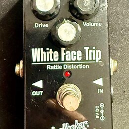 Černý kytarový efekt s nápisy White Face Trip a Rattle Distortion. Na horní straně jsou tři černé otočné ovladače s popisky Filter, Drive a Volume. V…