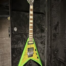 Zelená elektrická kytara s tělem ve tvaru V, položená v černém tvrdém kufru. Na hlavě je bílý nápis Jackson. Kytara má dva humbuckery, šest strun a h…