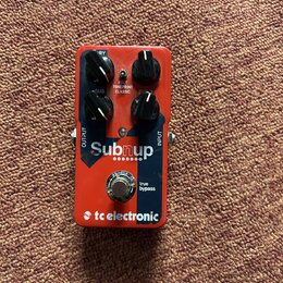 Červený kytarový efekt s nápisem Subnup a logem tc electronic. Na horní straně jsou čtyři černé ovládací knoflíky s popisky RY, SUB, TONEPRINT CLASSI…