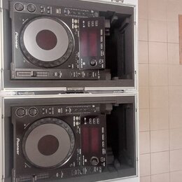 Dvě černé CDJ jednotky značky Pioneer umístěné v transportním kufru s hliníkovým profilem. Na obou zařizeních je viditelné logo Pioneer a nápis CDJ-1…