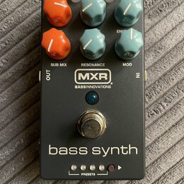Černý efekt pedál s nápisem bass synth a logem MXR BASS INNOVATIONS. Zařízení má šest ovládacích knoflíků v oranžové a modré barvě, stříbrný spínací…