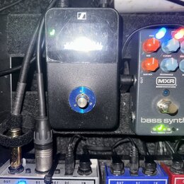 Černý efekt pedál s logem značky Sennheiser a jedním stříbrným knoflíkem uprostřed. Povrch je viditelně znečištěný prachem a drobnými škrábancemi. Ve…