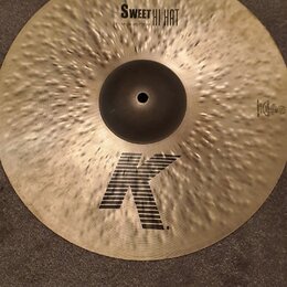 Zlatavý kovový činel s kladivkovaným povrchem. Na povrchu jsou černé nápisy SWEET HI HAT a 15"/38 cm BOTTOM, v dolní části velké logo K a vpravo nápi…