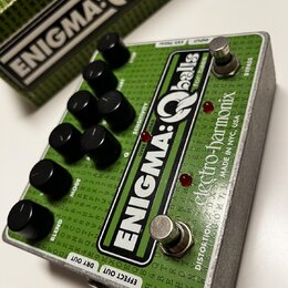 Zelený efekt pedál s nápisem ENIGMA:Qballs for Bass a značkou electro-harmonix MADE IN NYC, USA. Zařízení má osmi černých otočných knoflíků a dva sto…
