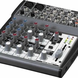 Míchací pult značky BEHRINGER, model XENYX 1002. Zařízení má šedý povrch s černými detaily, obsahuje řadu potenciometrů, posuvníků a vstupních konekt…
