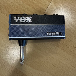 Černý kytarový efekt s nápisem VOX v horní části a Modern Bass na spodním modrém panelu s geometrickým vzorem. Zařízení má v dolní části integrovaný…