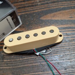 Kremově bílý humbucker s šesti viditelnými póly, vedoucími z něj čtyři barevné vodiče (červený, bílý, zelený a černý). Vedle nástroje je umístěna kra…