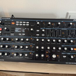 Černý polyfonní syntetizátor Novation Peak v dřevěném šasi. Na displeji je zobrazen text „Himalaya SS 1/1“, „raw“, „Category All“. Přední panel obsah…