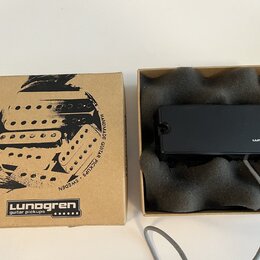 Kartonová krabice s černým potiskem a nápisy „Lunogren guitar pickups“ a „HANDMADE GUITAR PICKUPS · SWEDEN“. Vedle krabice je otevřené balení s černý…