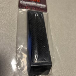 Černý obdélníkový blok s povrchem imitujícím karbonová vlákna, zabalený v průhledném plastovém sáčku. Na kartonové vložce je nápis SHRED NECK a pod n…