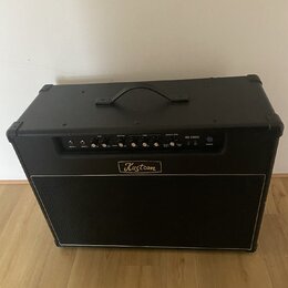 Černý kytarový kombo zesilovač s látkovým krytem reproduktoru. Na předním panelu je nápis Kustom v oválném rámečku a označení modelu KG 100FX. Horní…