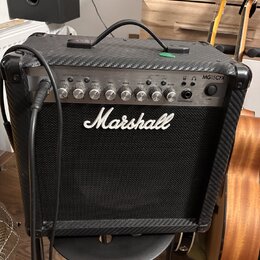 Kytarový kombo zesilovač značky Marshall, model MG15CFX. Má černý povrch s karbonovou texturou a stříbrný ovládací panel s několika otočnými knoflíky…