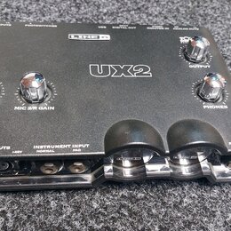 Černý zvukový interface Line 6 UX2. Na horní straně jsou čtyři chromované otočné ovladače s nápisy MIC 1/L GAIN, MIC 2/R GAIN, OUTPUT a PHONES. V pře…