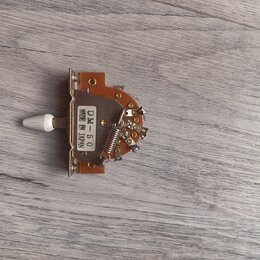 Kousek elektronického komponentu s bílým plastovým knoflíkem, umístěný na hnědém desce. Na bílém štítku je nápis DM-50 MADE IN JAPAN. Součást obsahuj…