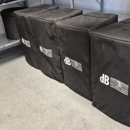 Pět černých transportních krytů z látky, které jsou umístěny v řadě na podlaze a polici. Na každém krytu je bílý nápis dB TECHNOLOGIES. Povrch látky…