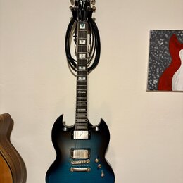 Elektrická kytara s modročerným přechodovým povrchem a tmavým hnedým hmatníkem. Na hlavě je bílý nápis Epiphone. Kytara má dva humbuckery, dva ovláda…
