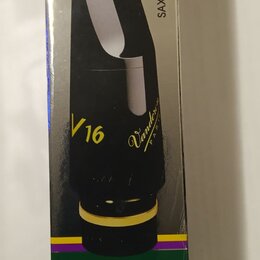 Krabice s obrázkem černého saxofonového phútu se zlatým prstencem u základny. Na krabici je svisle napsáno SAX. TENOR Sib - Bb a v dolní části zelený…