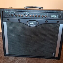 Černý kytarový kombo zesilovač s kovovou stříbrnou mřížkou. Na přední straně je nápis BANDIT 112 a logo Peavey. Horní ovládací panel obsahuje sekce I…
